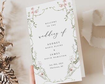 May include: A white wedding program card featuring a delicate watercolor botanical border of green vines and small pink flowers. The text reads: WELCOME TO THE wedding of AUDREY MARIE BLAIRE & JAMES DAVID HAMILTON July 19th, 2025 Charleston, SC.