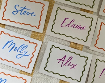 May include: A set of place cards with names written in cursive. The cards are decorated with a wavy border in different colors, including orange, green, and brown.