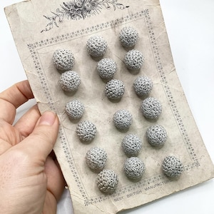 以下が含まれることがあります： 15個の銀色のボタンが並んだカード。カードには花柄のデザインと「BEST BRITISH MANUFACTURE」の文字が書かれている。