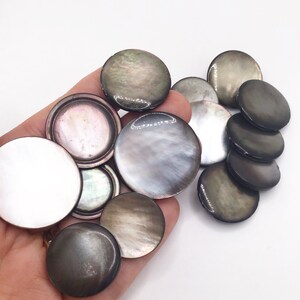 May include: A collection of round, iridescent, mother-of-pearl buttons in shades of grey, black, and white. The buttons have a smooth, polished finish and are perfect for adding a touch of elegance to any project.