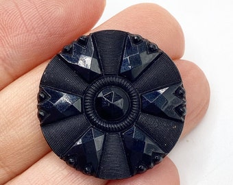 Puede incluir: Un botón de vidrio negro con un diseño de estrella. El botón tiene un centro elevado con un diseño de estrella más pequeño.