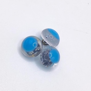 May include: Three clear glass buttons with a blue center and a silver-colored shank. The buttons are round and have a slightly domed shape. The blue color is vibrant and contrasts with the clear glass.