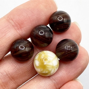 May include: Five round glass beads, four are brown with white stripes and one is white with brown stripes.
