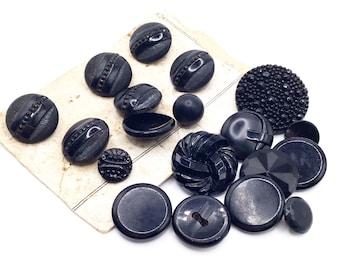 May include: A collection of black glass buttons in various shapes and sizes, including round, oval, and star-shaped buttons. Some buttons have a textured surface, while others are smooth.