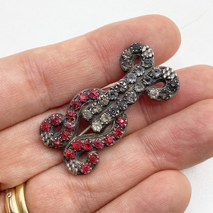 May include: A silver brooch with a stylised design set with red and clear rhinestones.
