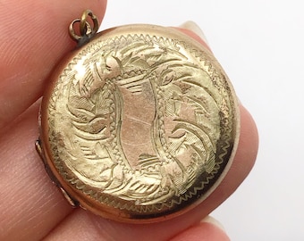 以下が含まれることがあります： 精巧な花柄と渦巻き模様の彫刻が施された、丸い金色のロケット。ロケットには装飾的な縁と、チェーン用の小さなループが付いています。デザインは、モノグラム用の可能性のある、中央の装飾のない領域が特徴です。