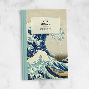 Puede incluir: Un libro con un diseño de ola azul y blanca en la portada. El título es "Bon Voyage!" y el autor es "Jack Smith".