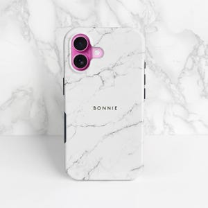 May include: White marble-effect phone case with a pink camera surround. The case features the name "BONNIE" printed in black. The phone case is designed to fit a smartphone.