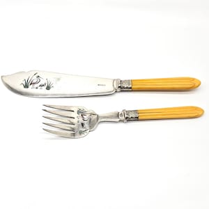 May include: A butter knife and fork set with silver blades and tines, and yellow handles. The knife blade features a decorative etched design of a bird and reeds. The set is on a white background.