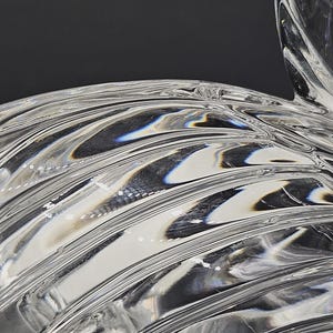 May include: Close-up of a clear glass object with a rippled, wave-like design. The glass has a glossy, reflective surface, with light and shadow creating depth and dimension. The object's form is abstract and artistic.