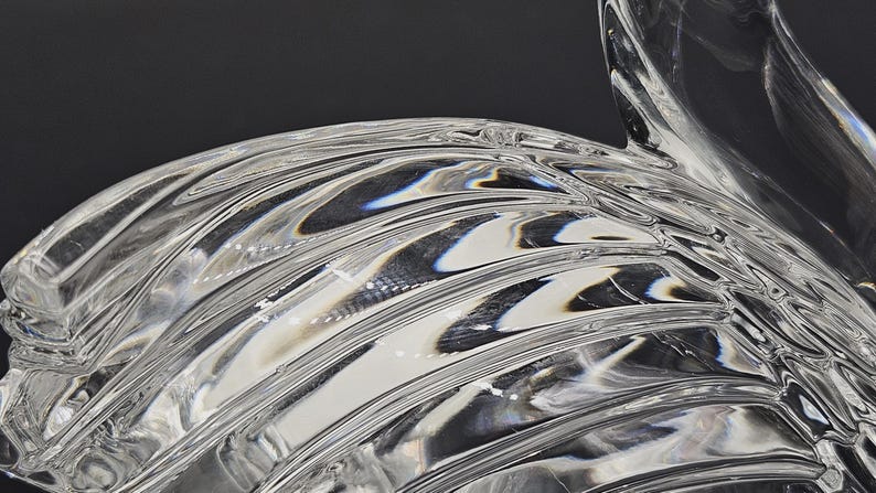 May include: Close-up of a clear glass object with a rippled, wave-like design. The glass has a glossy, reflective surface, with light and shadow creating depth and dimension. The object's form is abstract and artistic.