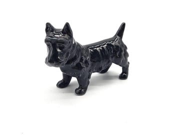 May include: A glossy black ceramic figurine of a Scottish Terrier dog. The dog is standing with its tail up and ears perked. The figurine has a smooth, reflective surface and is set against a white background.