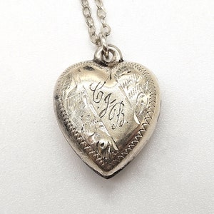 May include: Silver heart-shaped locket with an engraved design and the initials "G.J." on the front.