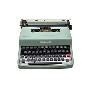 May include: A classic mint green typewriter featuring black keys and a red return key. The typewriter has a silver carriage and a label reading "Olivetti Lettera 32". The keys are arranged in a QWERTY layout.