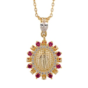 Puede incluir: Collar de cadena dorada con un colgante que representa a la Virgen María rodeada de un halo de pequeñas piedras preciosas blancas y rojas.