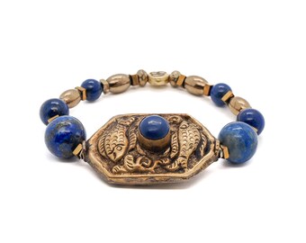 May include: A blue lapis lazuli beaded bracelet with a gold-toned pendant featuring two fish and a blue stone in the centre.