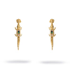 May include: A pair of gold-coloured alligator earrings. Each earring features a detailed alligator design with colourful gemstone accents. The earrings are set against a white background, highlighting their intricate craftsmanship and design.