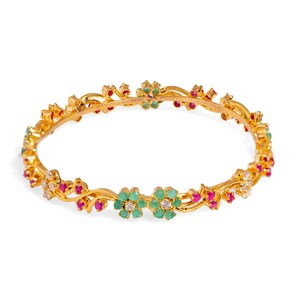 May include: A gold bangle bracelet with a floral design. The bracelet is adorned with green and red gemstones.