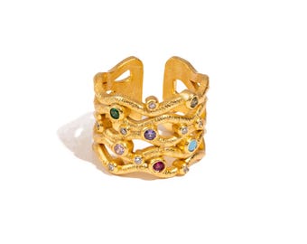 May include: Gold-coloured adjustable ring with a textured design. The ring features multiple layers adorned with colourful gemstones, including green, purple, pink, red, and turquoise, along with clear crystals. The ring is set against a white background.