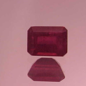 May include: A deep red gemstone with a square shape and a slightly rounded edge. The gemstone is reflecting light, creating a subtle shine.
