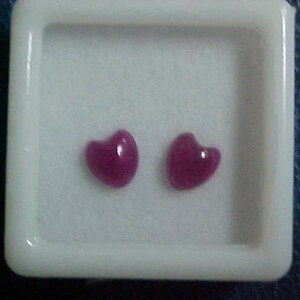 May include: Two pink heart-shaped gemstones in a white square box.