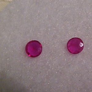 Könnte beinhalten: Zwei runde, rosafarbene Edelsteine auf weißem Hintergrund.