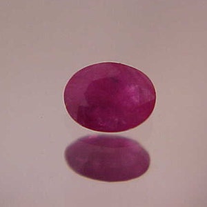May include: A deep pink oval-shaped gemstone with a smooth, polished surface.