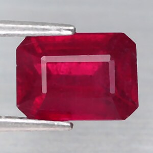 May include: A deep red ruby gemstone with a rectangular emerald cut.