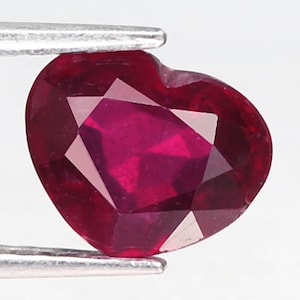 以下が含まれることがあります： ファセットカットされたハート型の濃い赤色のルビーの宝石です。