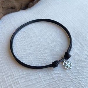 May include: A black adjustable bracelet with a silver four-leaf clover charm.