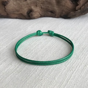 May include: A green braided cord bracelet with a simple knot closure.