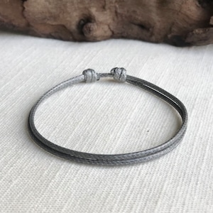 May include: A simple gray string bracelet with a double knot closure.