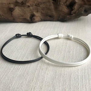 May include: Two friendship bracelets, one black and one white, made of thin cord, tied in a simple knot.
