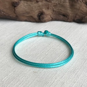 May include: A turquoise blue braided string bracelet with a simple knot closure.