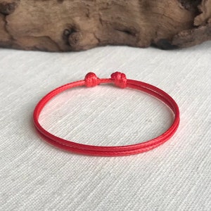 May include: A red string bracelet with a simple knot design. The bracelet is made of a thin, durable cord and is adjustable to fit most wrists.