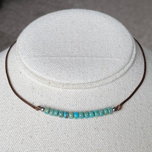May include: A turquoise beaded necklace with silver accents on a brown leather cord.