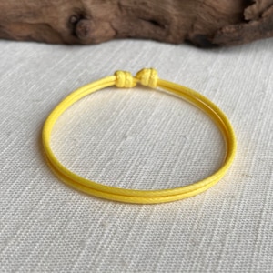 May include: A yellow braided cord bracelet with a simple knot closure.