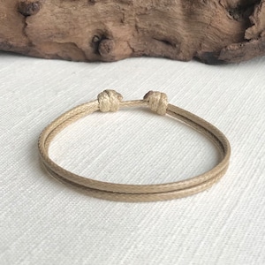 May include: A simple beige braided rope bracelet with a knotted closure.