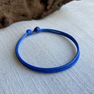 May include: A simple blue string bracelet with a knotted closure.