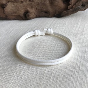 May include: A white braided rope bracelet with a simple knot closure.