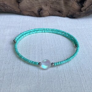 May include: A delicate turquoise beaded bracelet with a single iridescent white bead in the center.