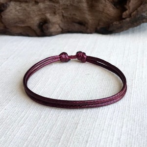 May include: A simple burgundy red string bracelet with a knotted closure.