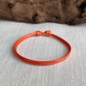 May include: A simple orange string bracelet with a knotted closure.