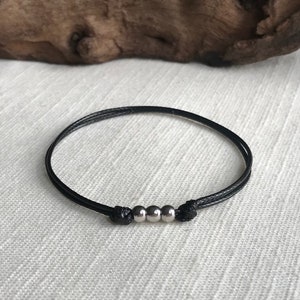 May include: A black string bracelet with three silver beads.