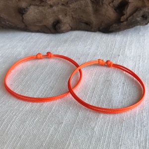 May include: Two orange string bracelets with a simple knot design.