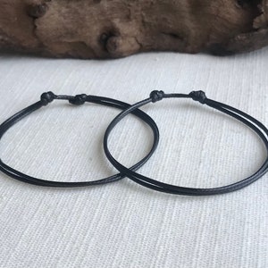 May include: Two black string bracelets tied in a knot.
