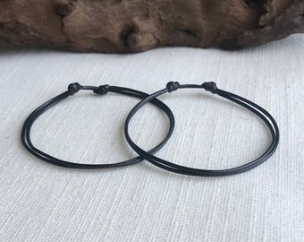 May include: Two black string bracelets tied in a knot.