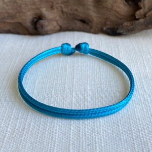 May include: A turquoise blue braided cord bracelet with a simple knot closure.