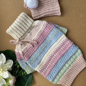 May include: A multi-colored striped knitted sweater with a high collar and a matching knitted hat with a white pom-pom. The sweater has a light pink, light blue, light green, and white color scheme. The text "@Lelina_mama" is visible in the bottom right corner of the image.
