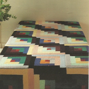 Op de afbeelding: Een veelkleurige deken met geometrisch patroon. De deken heeft een patchwork-ontwerp met rechthoekige blokken in verschillende kleuren, waaronder zwart, bruin, groen, blauw en beige. De deken is waarschijnlijk gemaakt van een zacht, geweven materiaal.